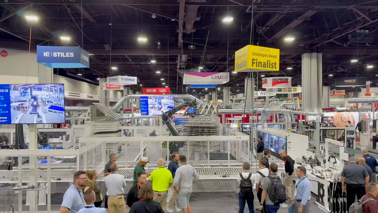 A crowd of attendees watching a full automated panel production line on the IWF 2026 show floor, with a robotic arm, conveyors, and an “IWF 2026 Challengers Award Finalist” banner overhead.